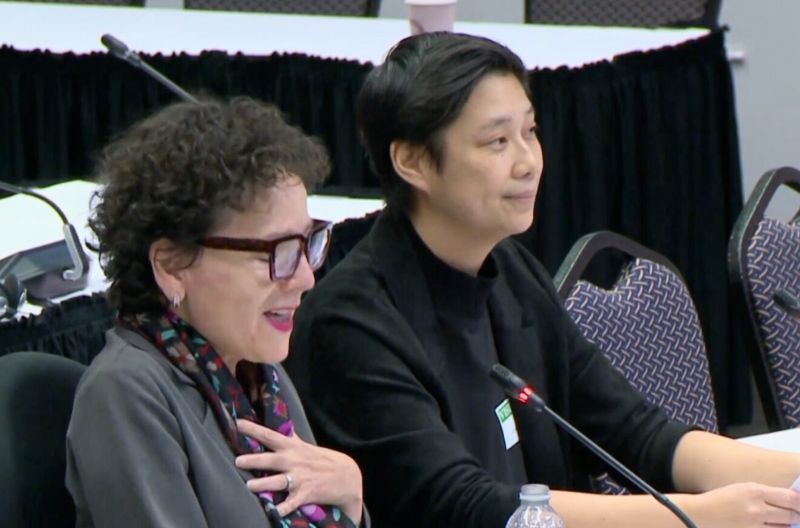 Yazmine Laroche and Winnie Luk speak at a microphone during a CRTC hearing. Yazmine is smiling with her hand over her chest, and Winnie sits beside her, listening attentively.