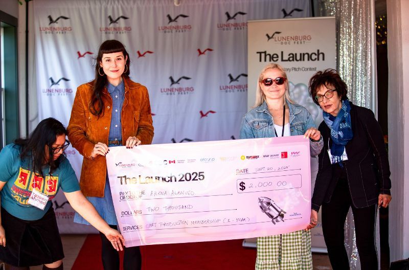 Four people stand together holding an oversized cheque.