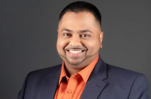 Portrait de Kenneth Mohabir, vêtu d'un blazer bleu et d'une chemise orange